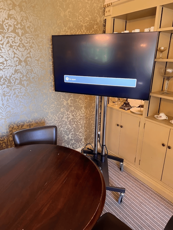 A mounted TV screen with No signal in an event setup room, alongside a wooden table and elegant decor.