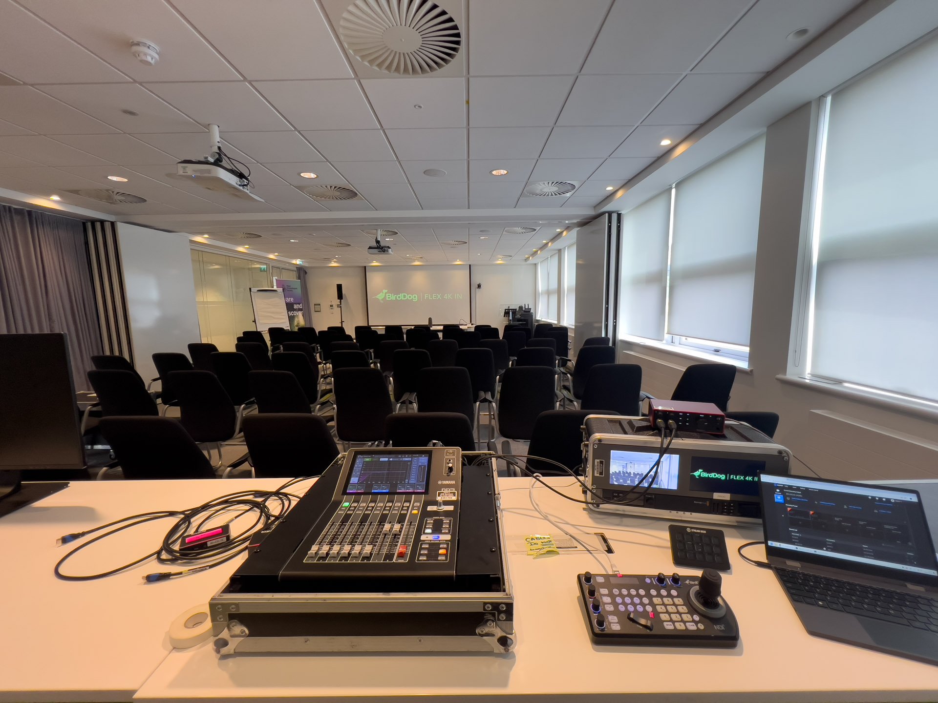 Audio-visual setup for a corporate conference, featuring a sound mixer, control panel, and projector in a modern meeting room.