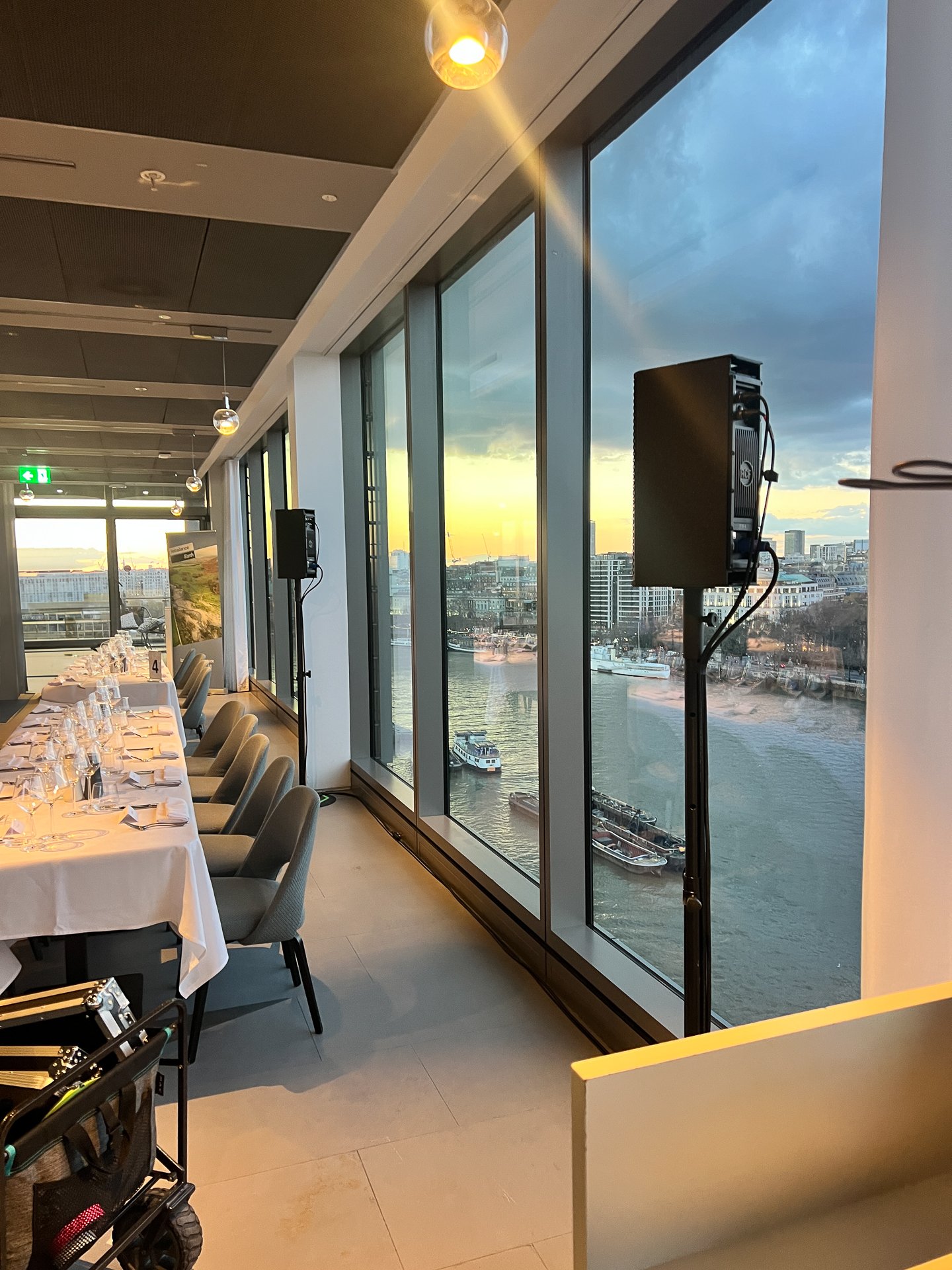 Event setup with dining table and sound equipment overlooking a river view at sunset, ideal for corporate gatherings.