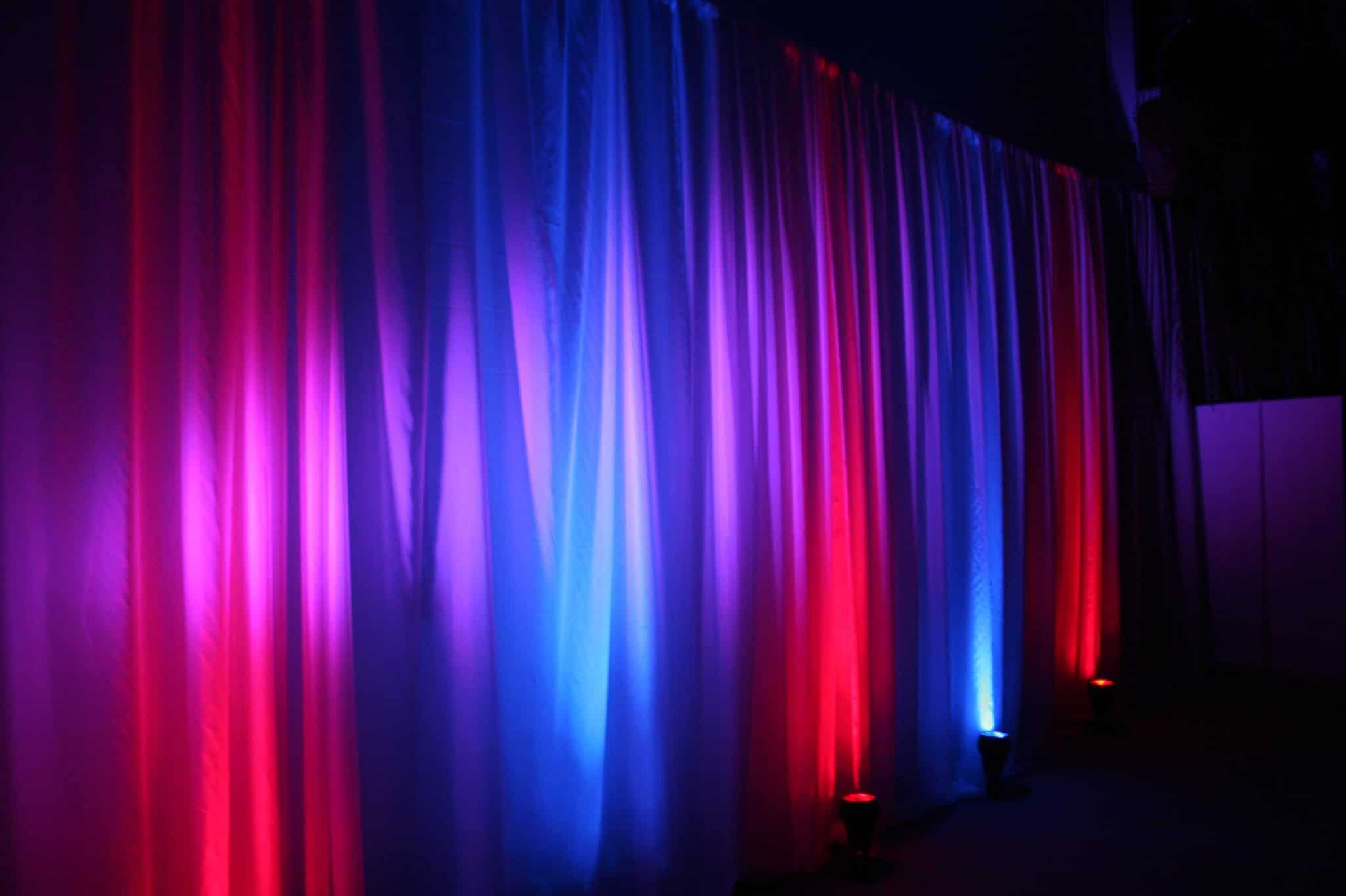 Stage drapes illuminated with red and blue uplighting for a corporate event, creating vibrant color effects.