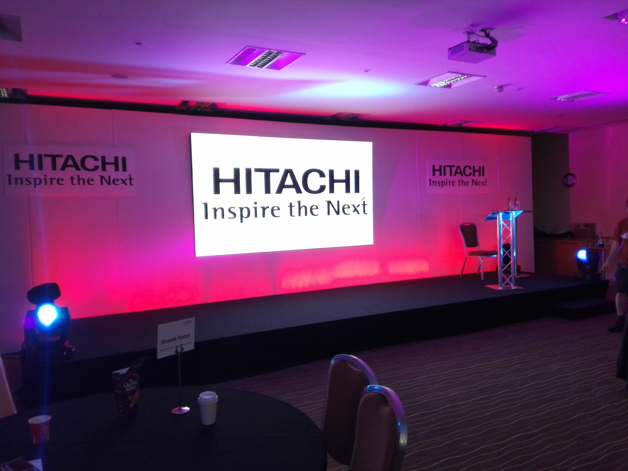Stage setup for a corporate event with branded backdrop, lighting effects, and podium.