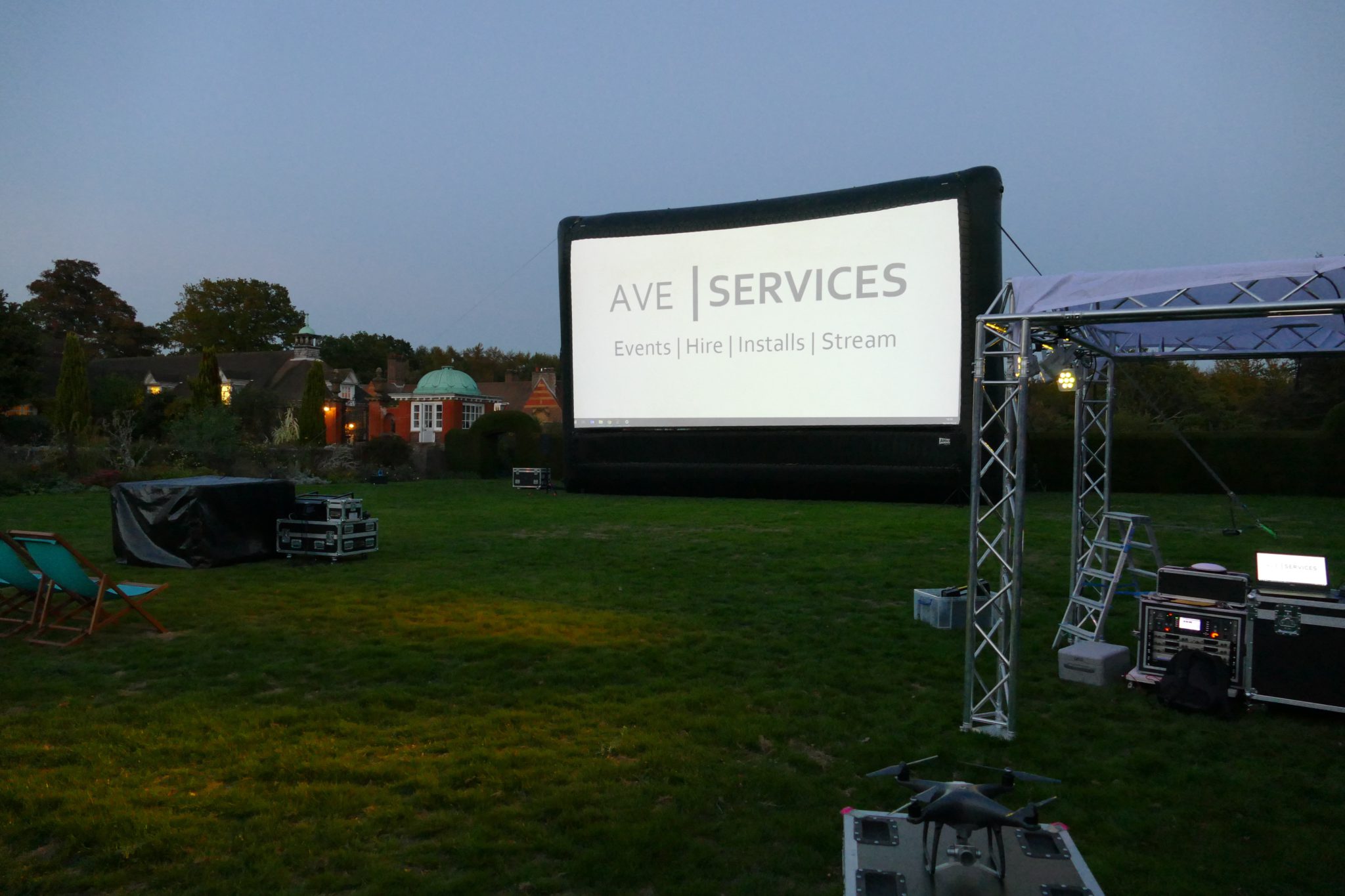 Outdoor cinema setup on a lawn with large AV screen, truss structure, and sound equipment, ideal for evening events.