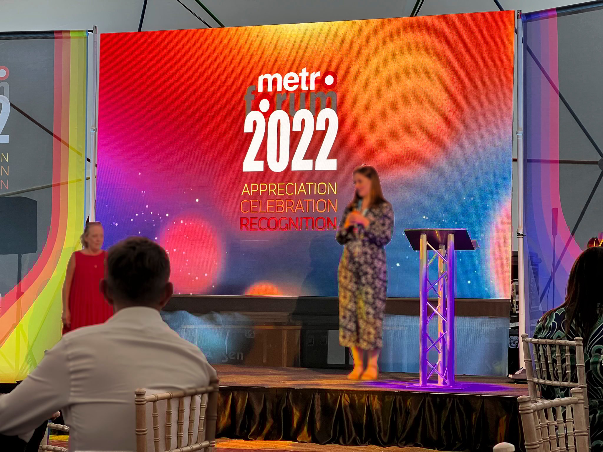 4m wide LED videowall for a corporate award show and after party. People on stage giving awards and a speech, next to a silver truss lectern