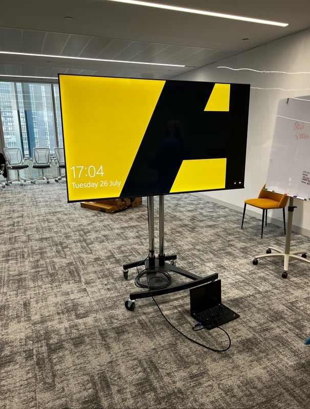 Large display screen on a mobile stand connected to a laptop in a conference room setup.