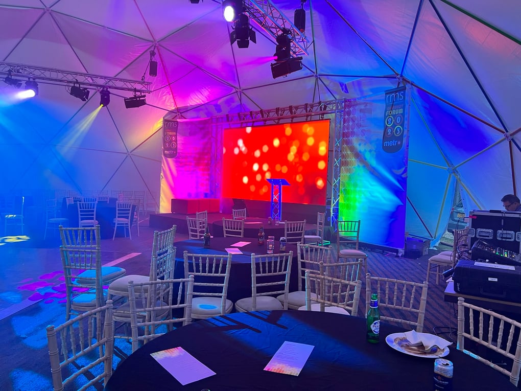 Geodesic dome setup with colorful stage lighting, large LED screen, seating, and AV equipment for a corporate event.