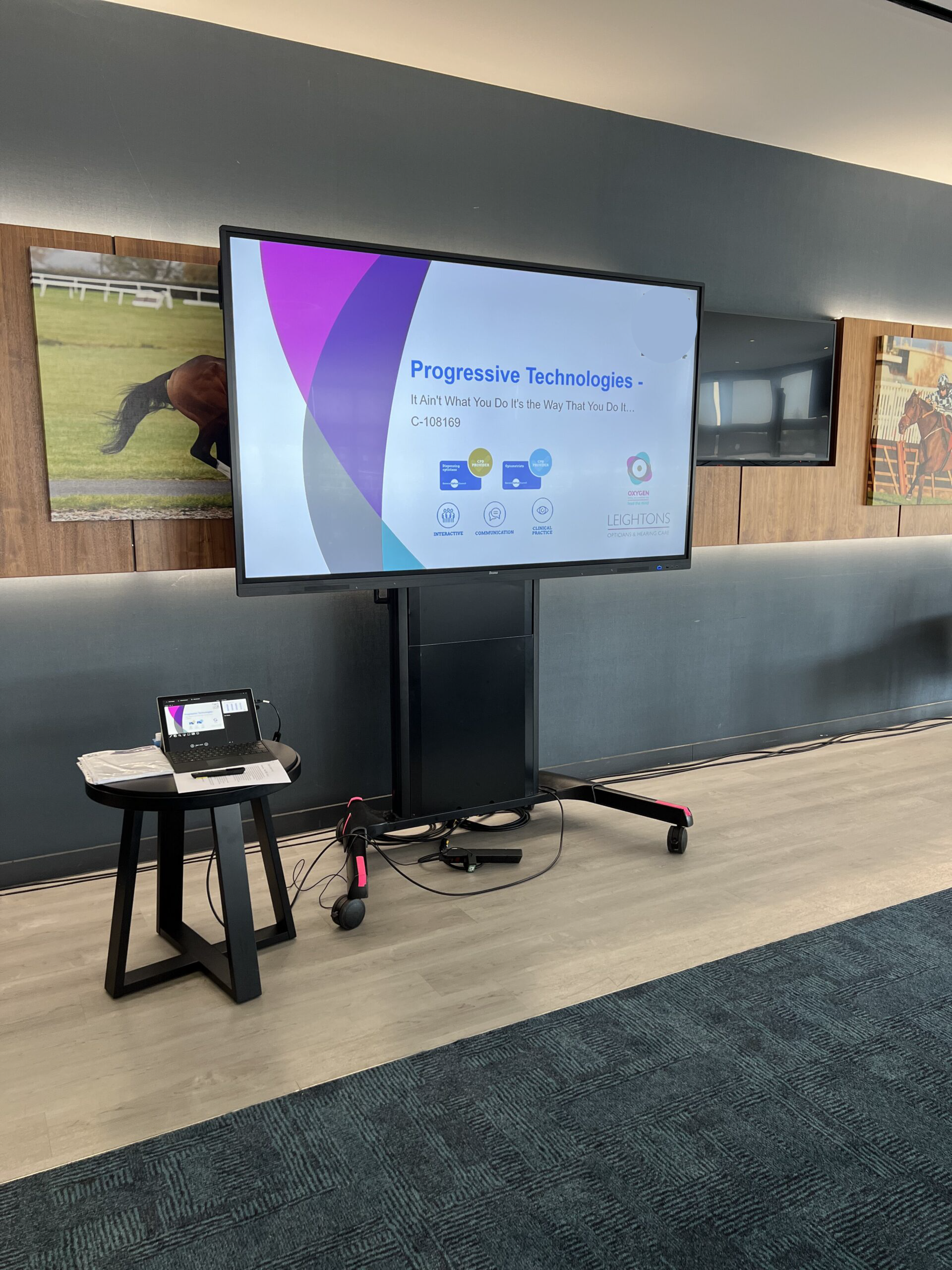Conference room presentation setup with a large touch screen displaying Progressive Technologies. Laptop and cables on the side table.