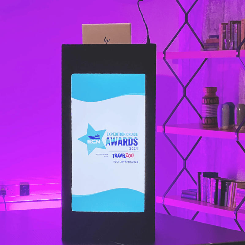 Podium with laptop and display showcasing Expedition Cruise Awards 2024 branding, set against purple event lighting.