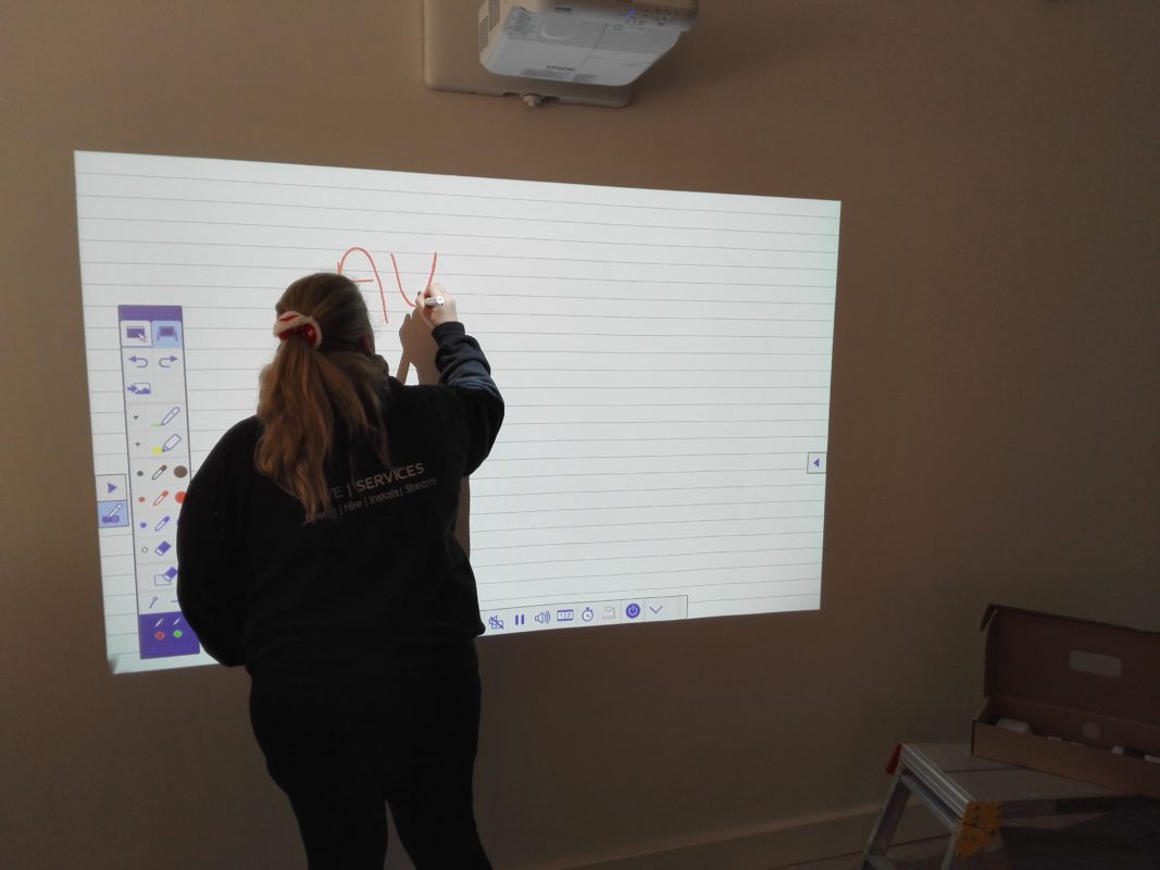 Person writing on interactive whiteboard with AV equipment setup for a conference or workshop setting.