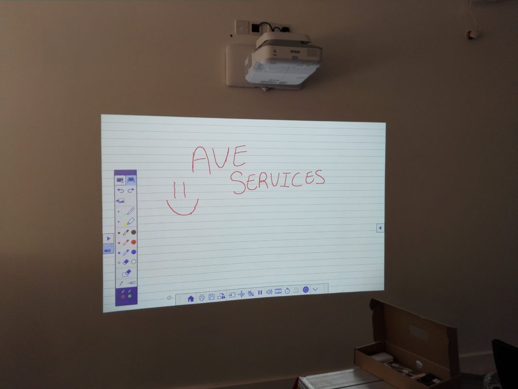 Projected whiteboard with AVE Services displayed in a meeting room setup, featuring digital drawing tools.