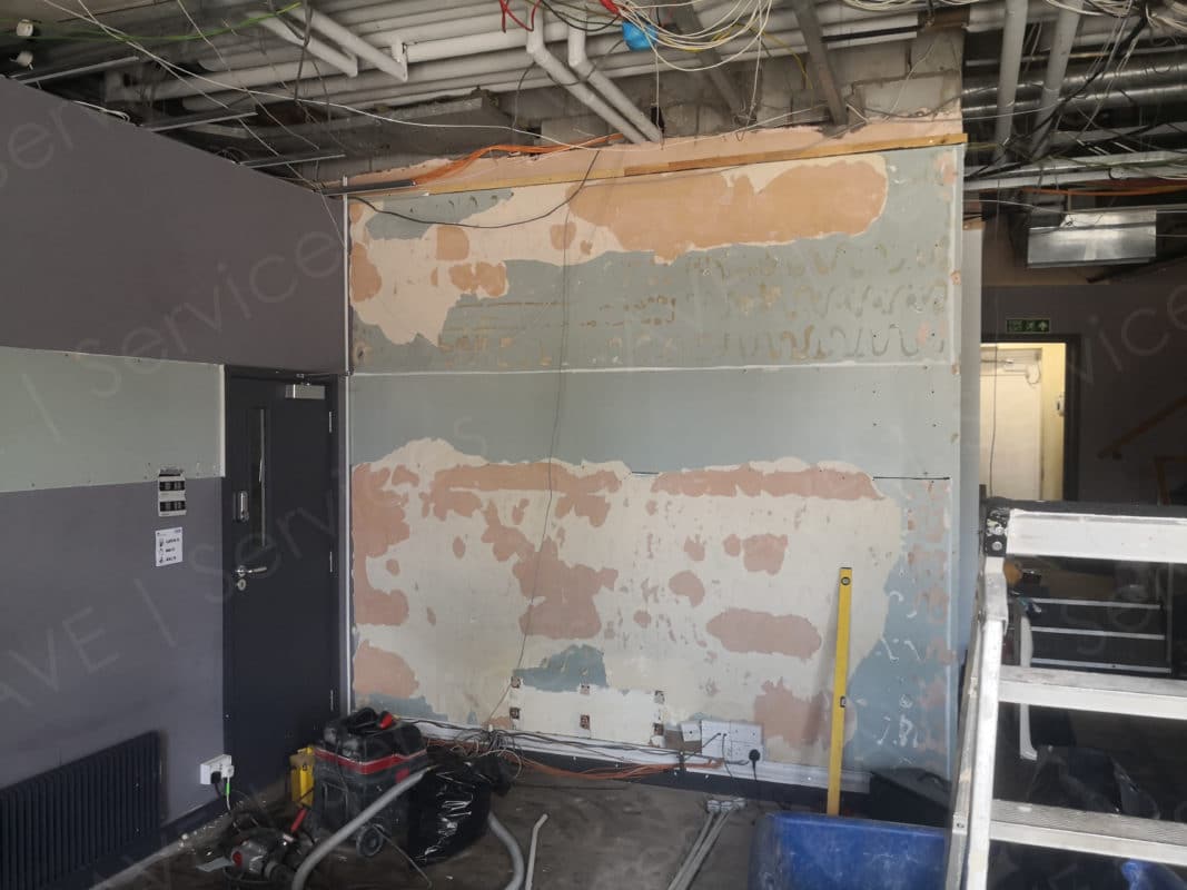 Venue under construction with exposed wiring and unfinished walls, featuring event setup equipment like a vacuum and ladder.