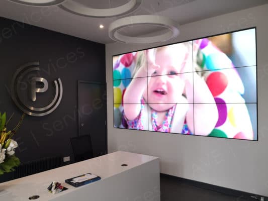 Reception area with a wall-mounted video display showing a baby, featuring modern AV setup and branded decor.